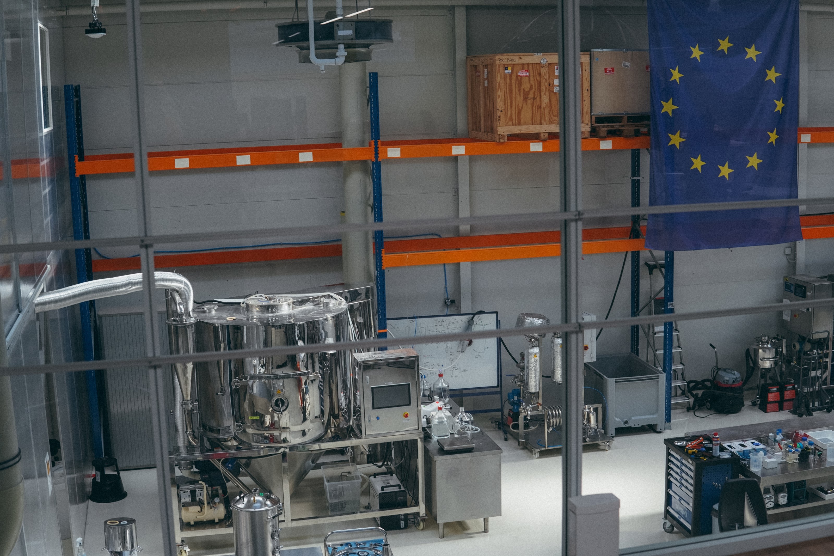 Steel fermentation vessels along the wall of the brewery, under the EU flag.